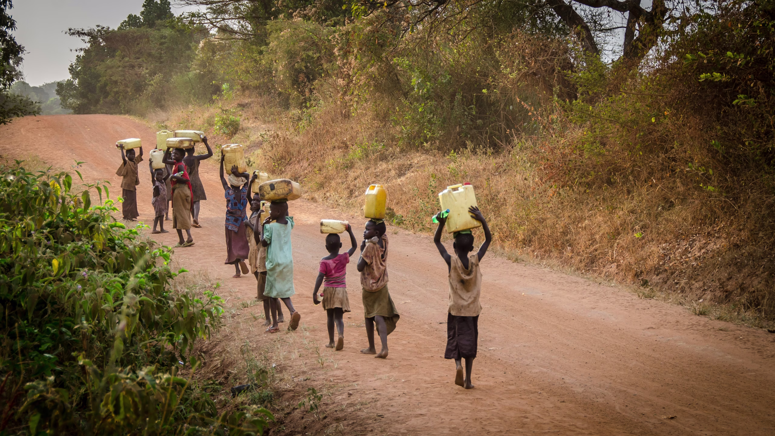 children carrying water on a dry road due to water shortages in Africa